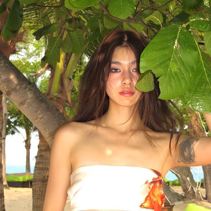 a woman in a white dress standing under a tree with her arm wrapped around the neck