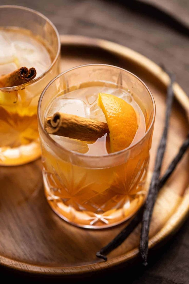 two glasses filled with drinks sitting on top of a wooden tray