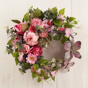 a wreath with pink flowers and butterflies hanging on a white wooden wall next to a door