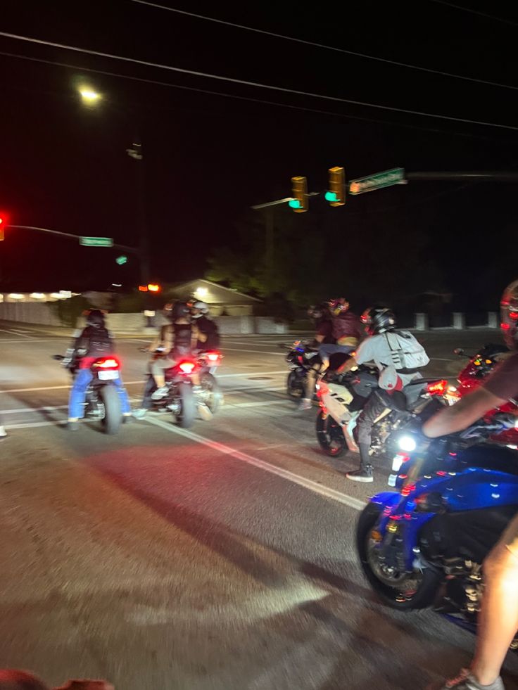 a group of bikers riding down the street at night with traffic lights in the background