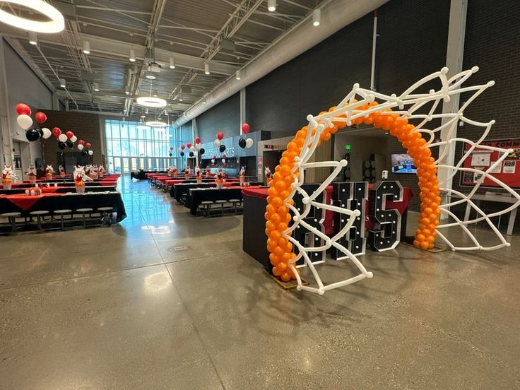 an orange and white balloon arch in the middle of a room with tables set up for a party