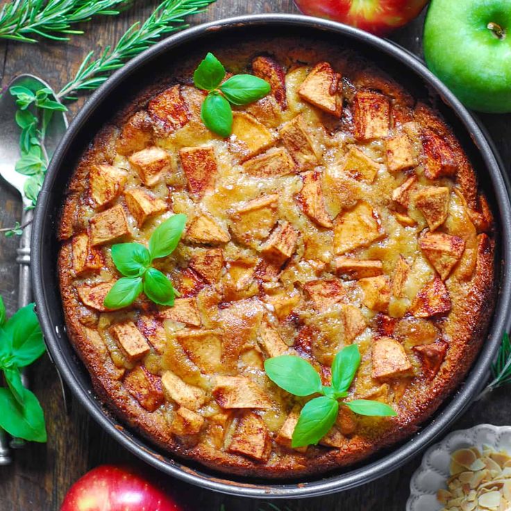 an apple pie with fresh green leaves on top and apples in the background next to it