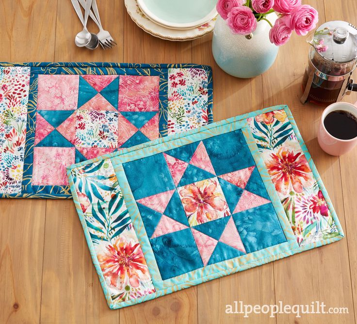 two quilted placemats sitting on top of a wooden table next to a cup of coffee