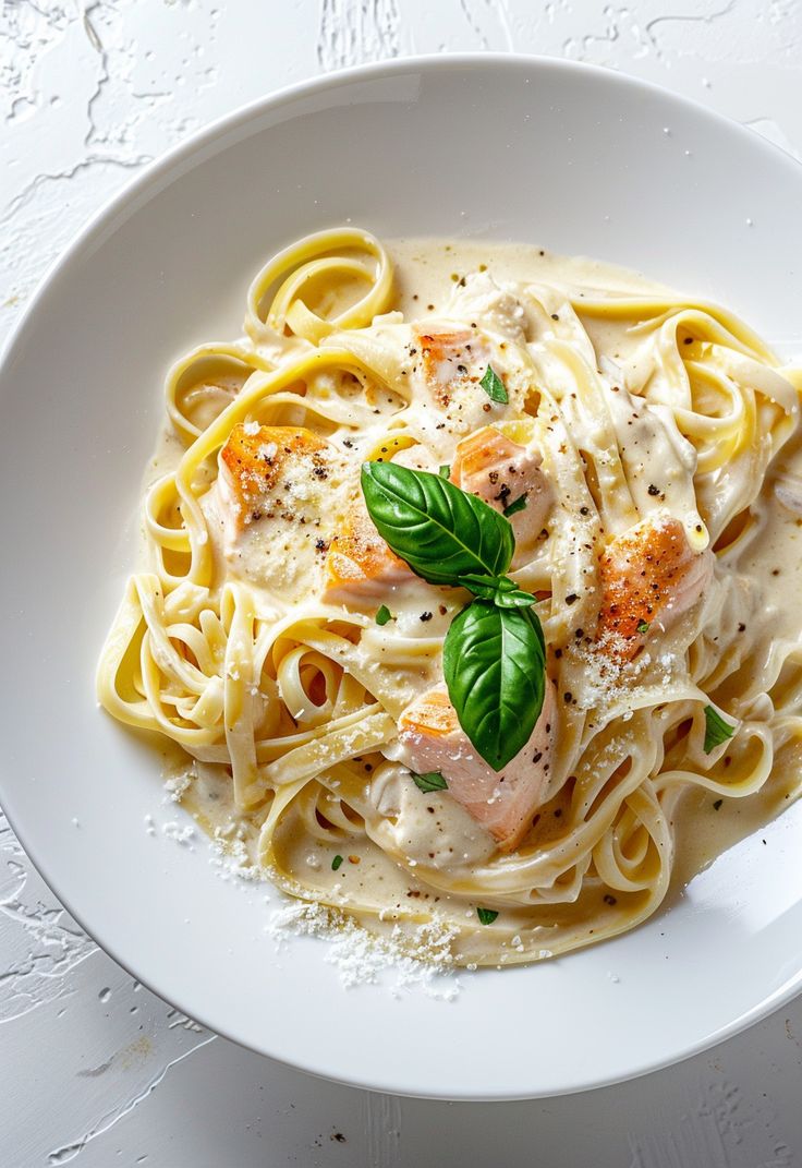 a white plate topped with pasta covered in sauce and garnished with green leaves