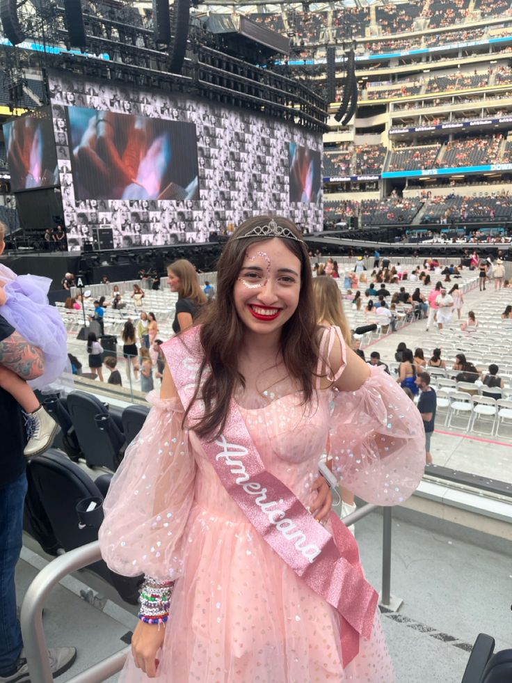 a woman in a pink dress at a stadium wearing a tiara and smiling for the camera