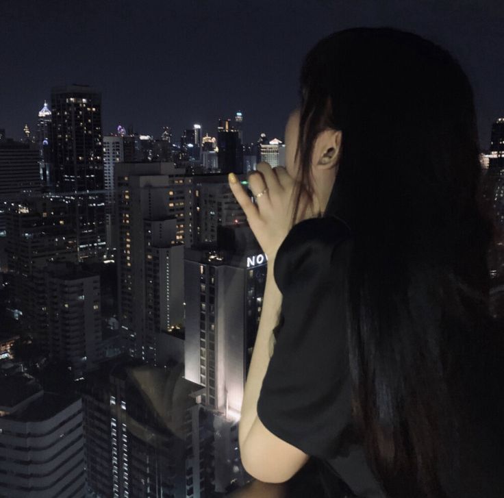 a woman standing on top of a building looking at the city lights in the distance