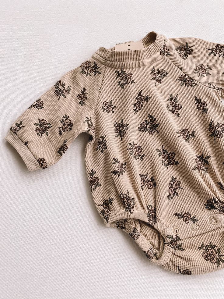 a baby's bodysuit laying on top of a white surface with flowers all over it