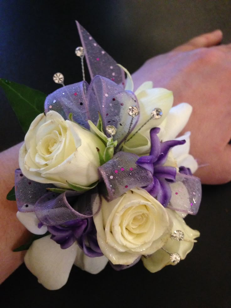 a bridal bouquet with white roses and purple orchids is being held by someone's hand