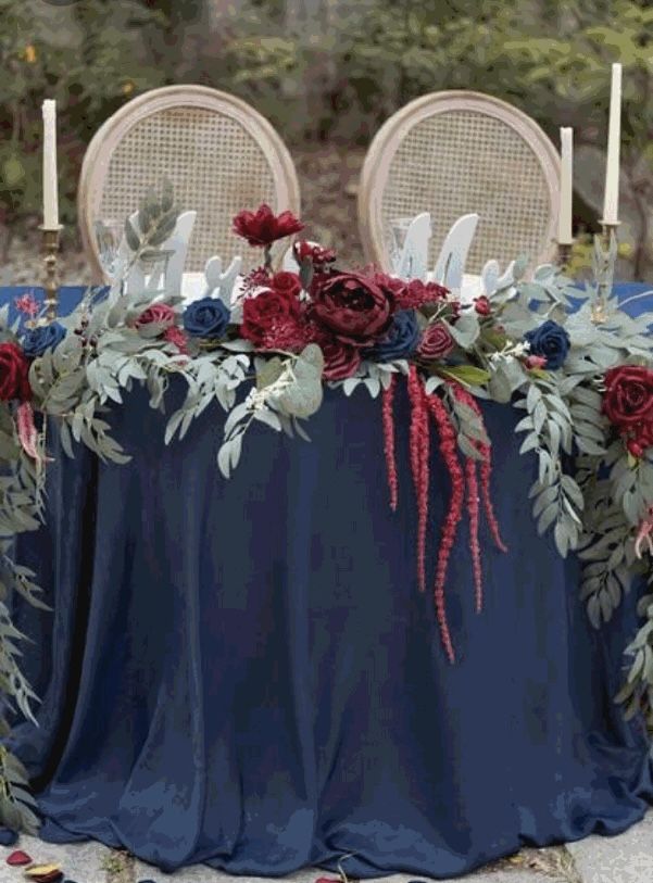 the table is decorated with red and blue flowers, greenery, and white candles