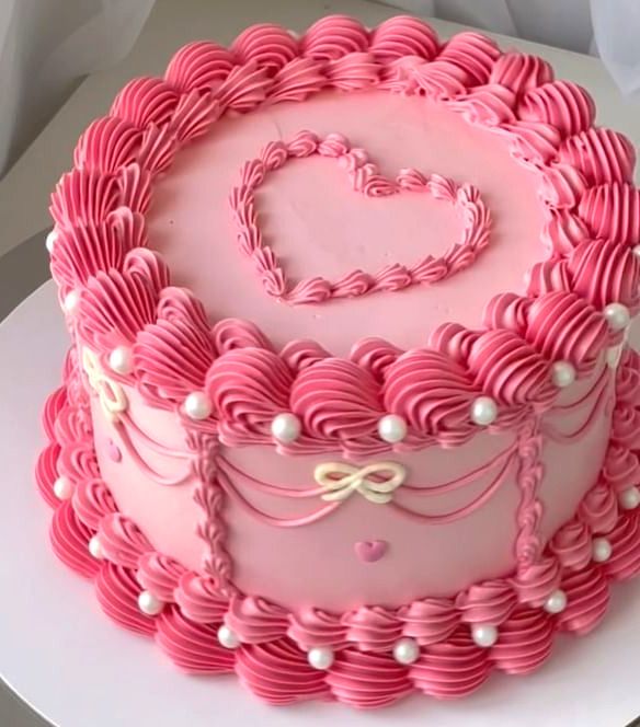 a heart shaped cake with pink icing and pearls on it's edges, sitting on top of a white plate