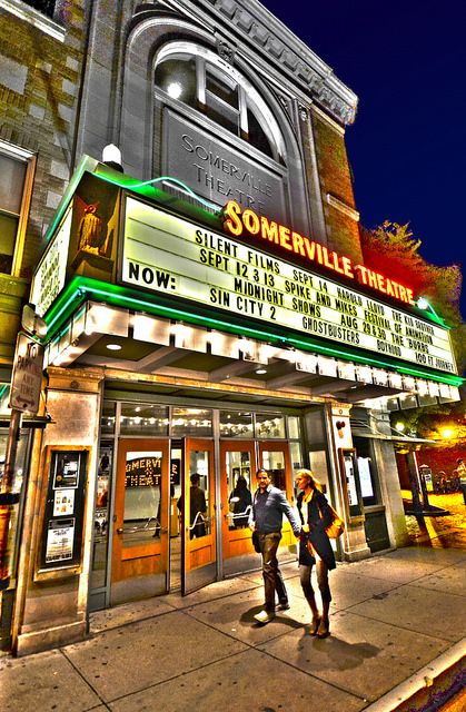 some people are walking on the sidewalk in front of a theater