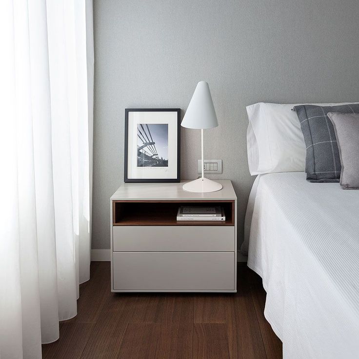 a white bed sitting next to a night stand on top of a wooden floor