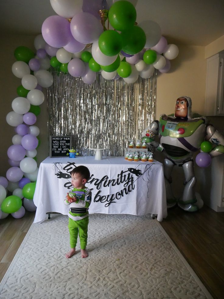 a little boy standing in front of a table with balloons on it and an image of buzz lightyear