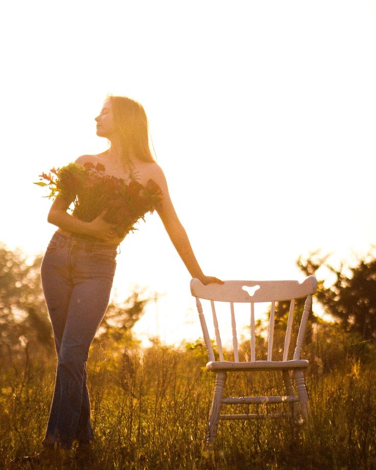 a woman standing next to a white chair in a field with flowers on her chest