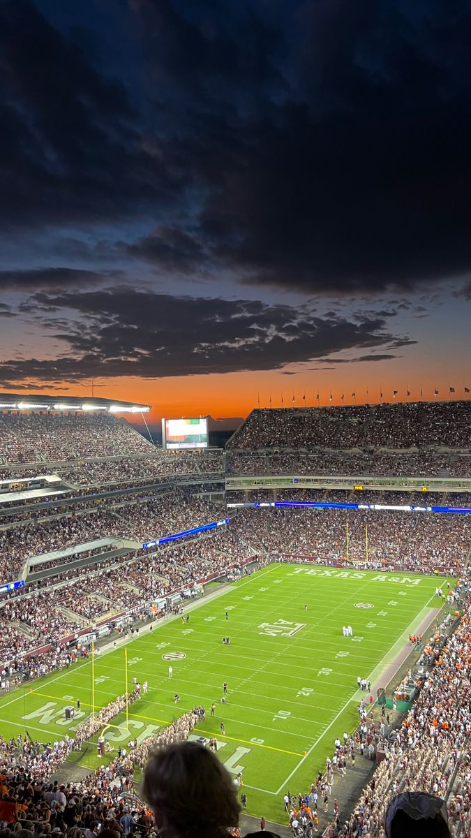 a stadium filled with lots of people watching a football game at sunset or dawn in the evening