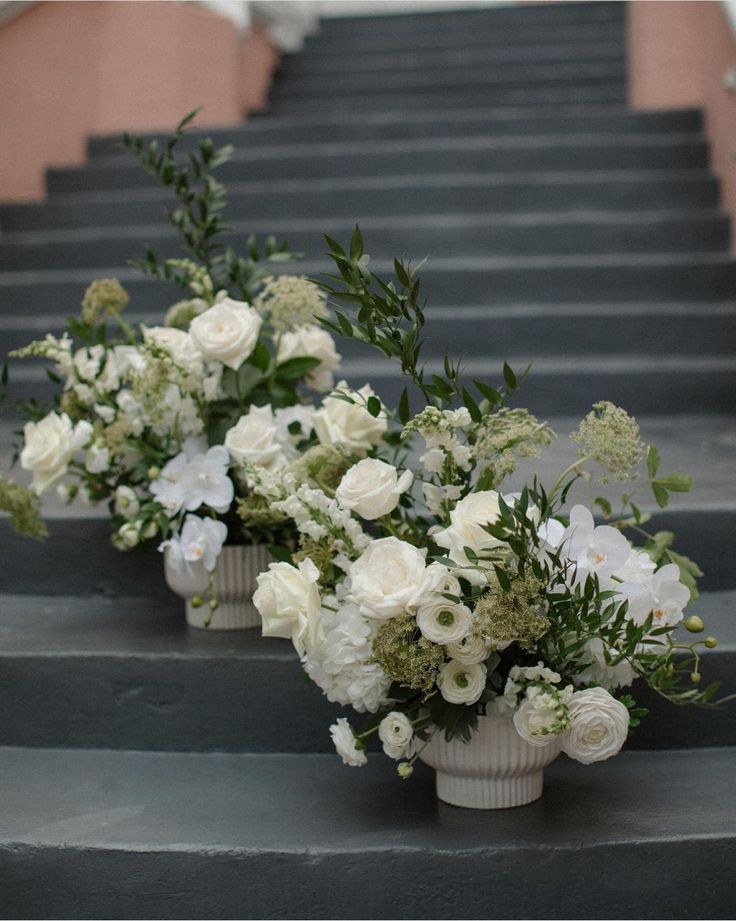 three vases filled with white flowers sitting on the steps