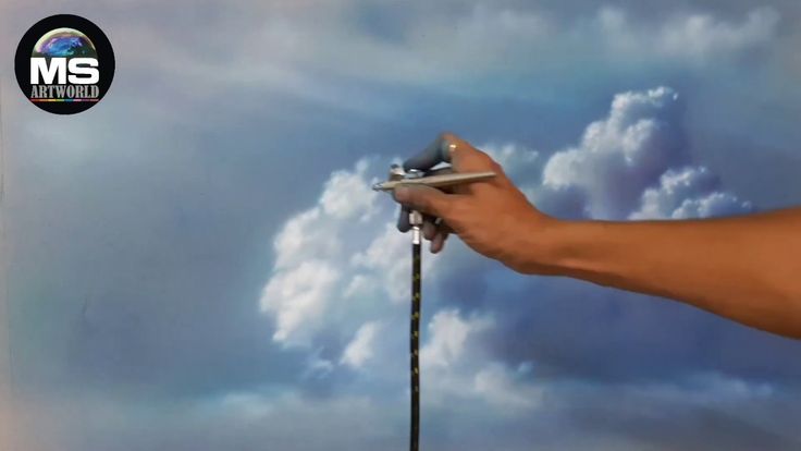 a hand holding a pair of scissors in front of a painting of clouds and blue sky