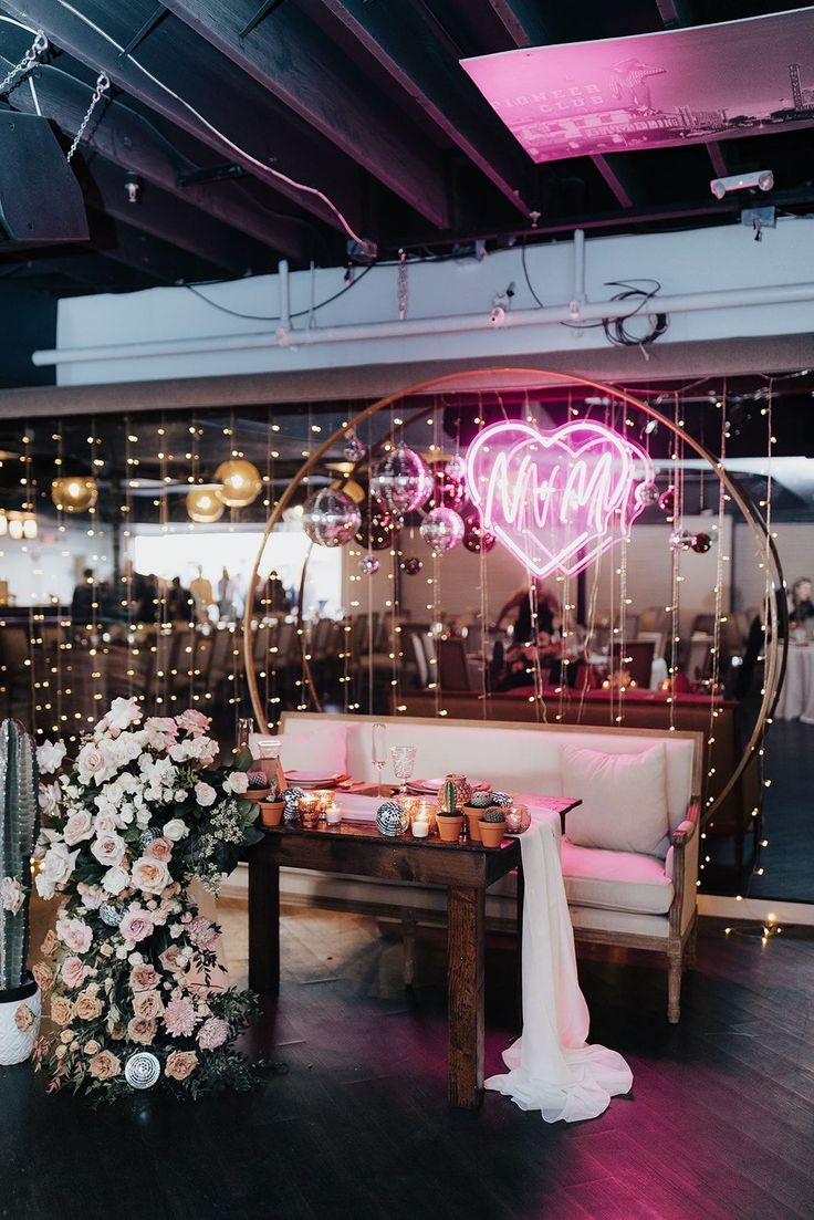 a table with flowers and candles in front of a neon sign