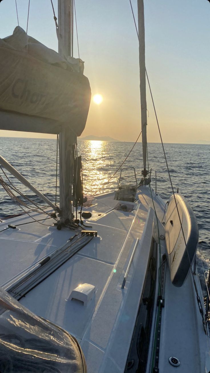 the sun is setting over the ocean on a sailboat