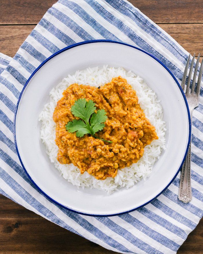 a white plate topped with rice covered in curry and garnished with cilantro