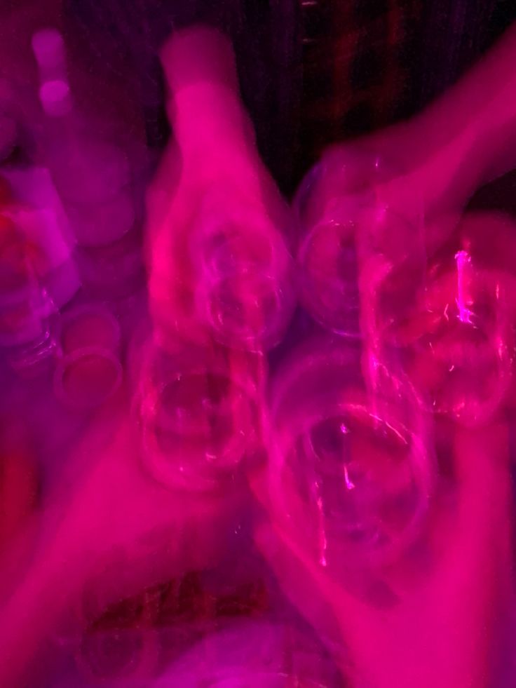 two hands holding wine glasses in front of purple and pink light, with other people's hands reaching for them