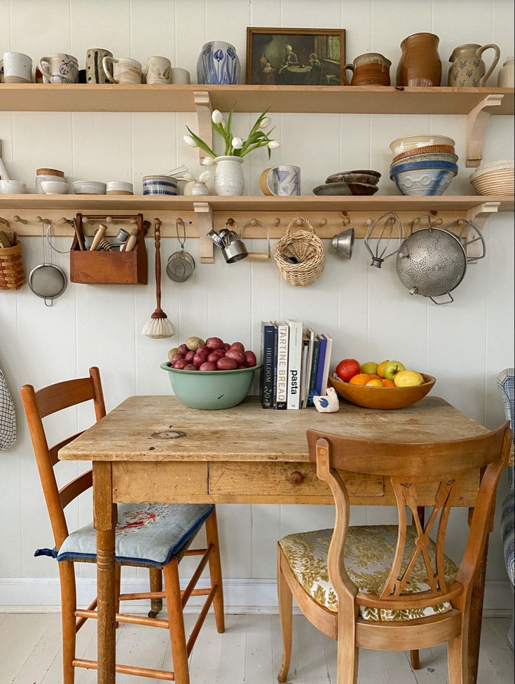 a wooden table topped with fruit and bowls next to a shelf filled with pots and pans