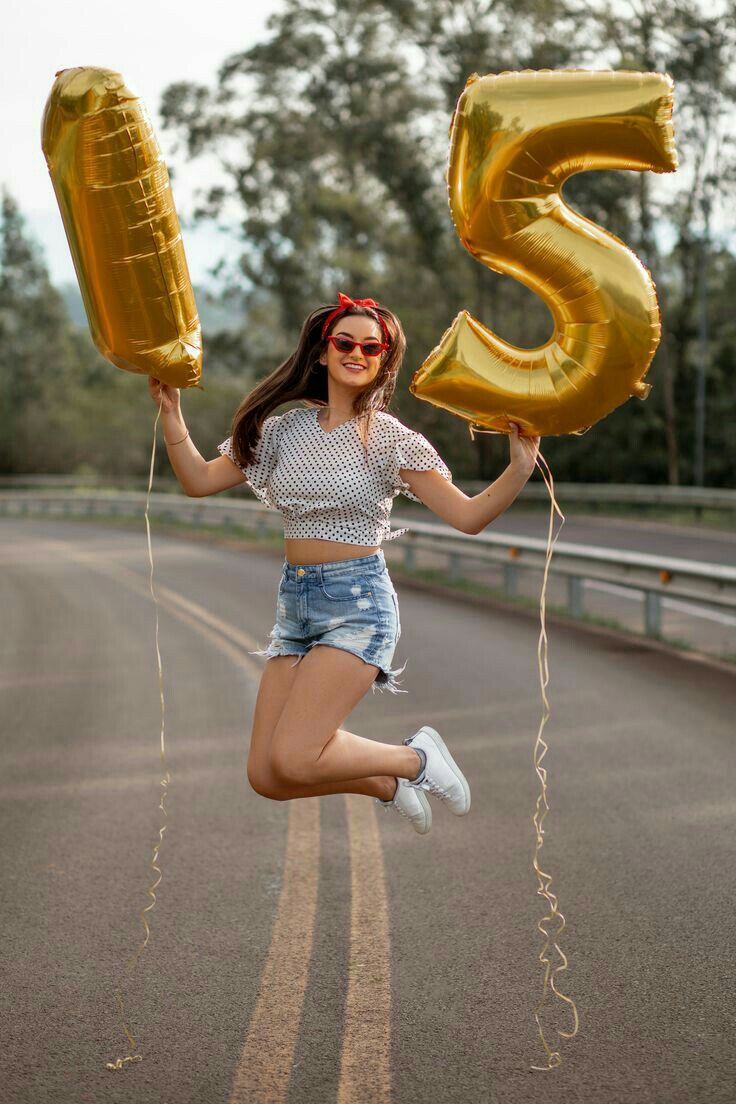 a woman is jumping in the air with balloons and number 5 on her feet while holding two large gold balloons