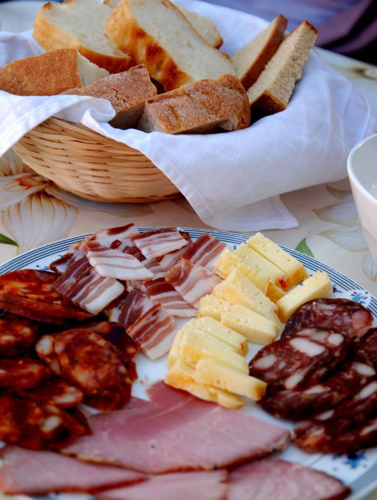 an assortment of meats and cheeses on a plate with bread in the background