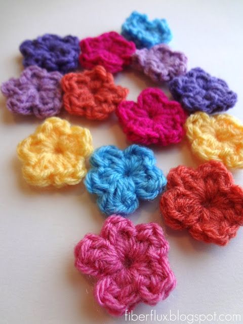 small crocheted flowers are arranged on a white surface, with the colors red, yellow, purple, and blue