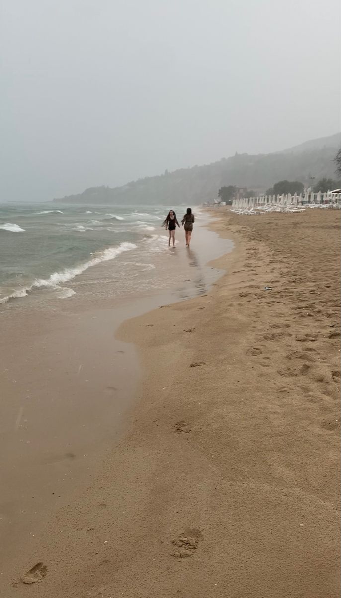 two people are walking along the beach on a foggy day