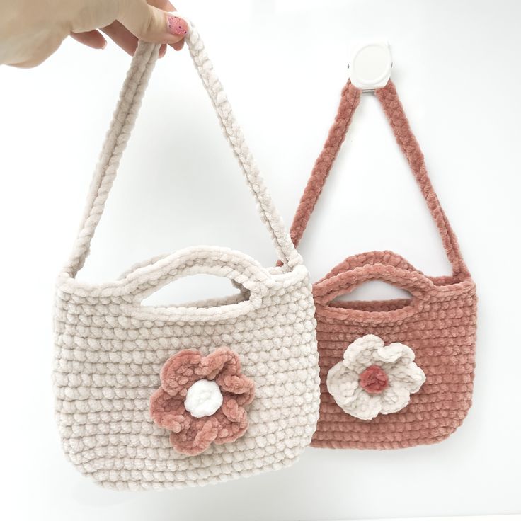 two crocheted purses being held by someone's hand on a white surface