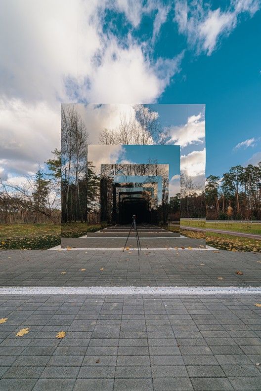 a person standing in front of a large mirror on the side of a road next to trees