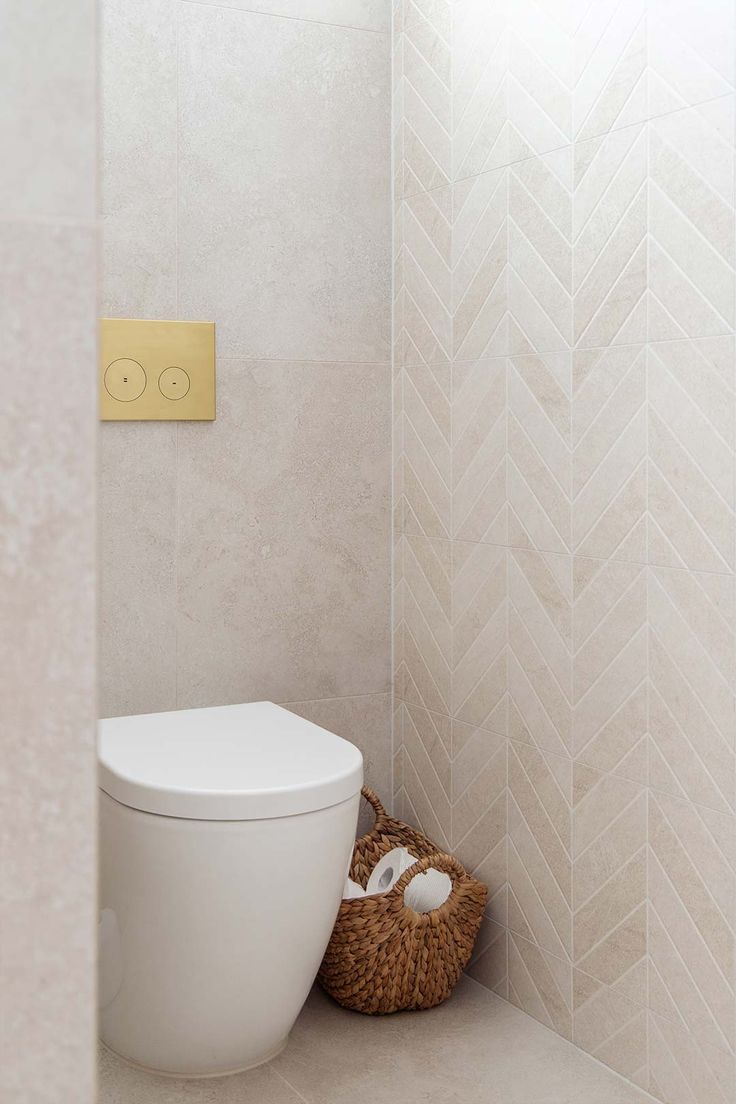 a white toilet sitting in a bathroom next to a basket on the floor and a light switch