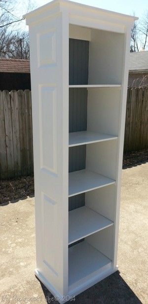 an empty white bookcase sitting on top of a cement ground next to a fence