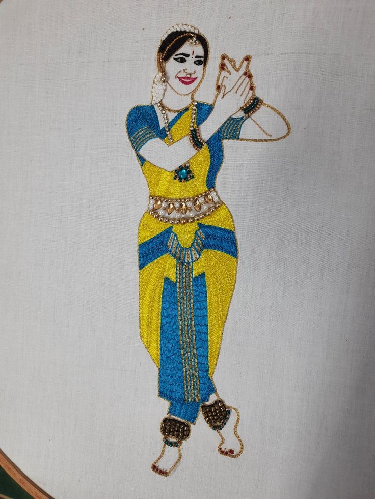 a woman in yellow and blue is embroidered onto a white piece of cloth with gold trim