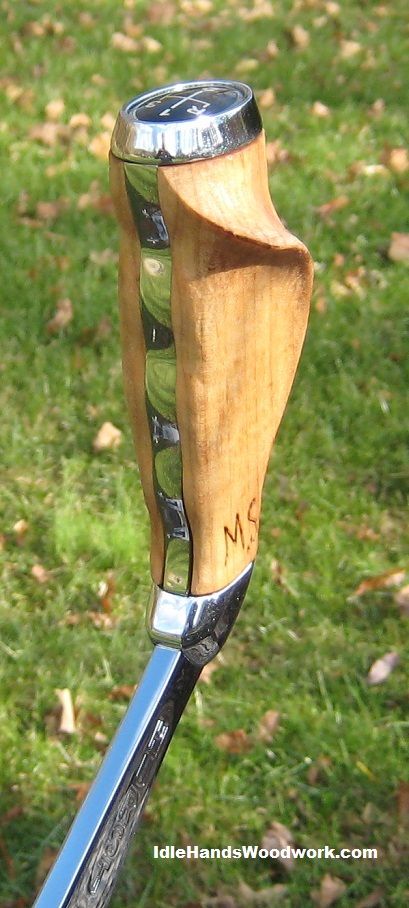 a close up of a wooden handle on a metal pole with grass in the background