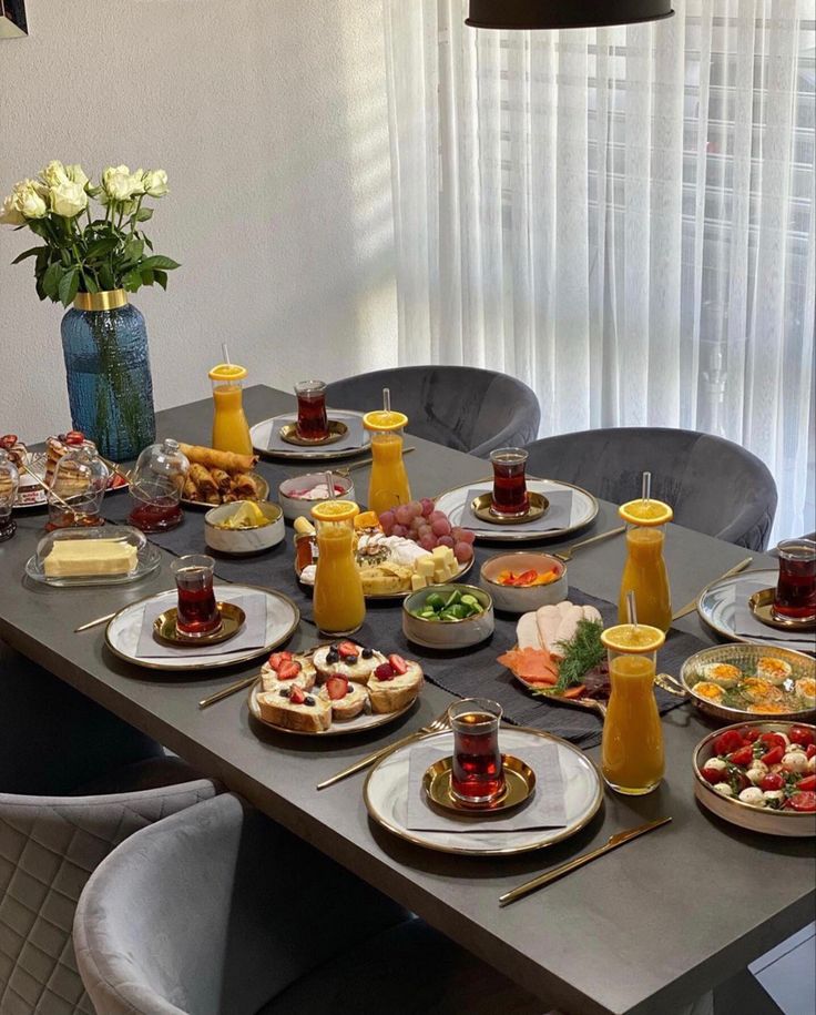 a long table with plates and bowls of food on it, along with vases filled with flowers