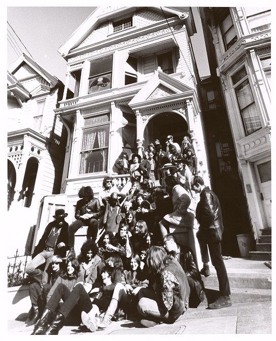 a group of people sitting on the sidewalk in front of a house