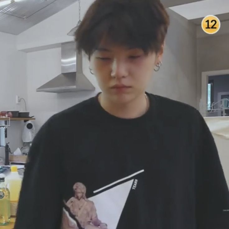 a young man standing in a kitchen wearing a black shirt with an image on it