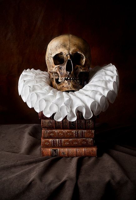 a skull sitting on top of two books in front of a black background with white ruffles