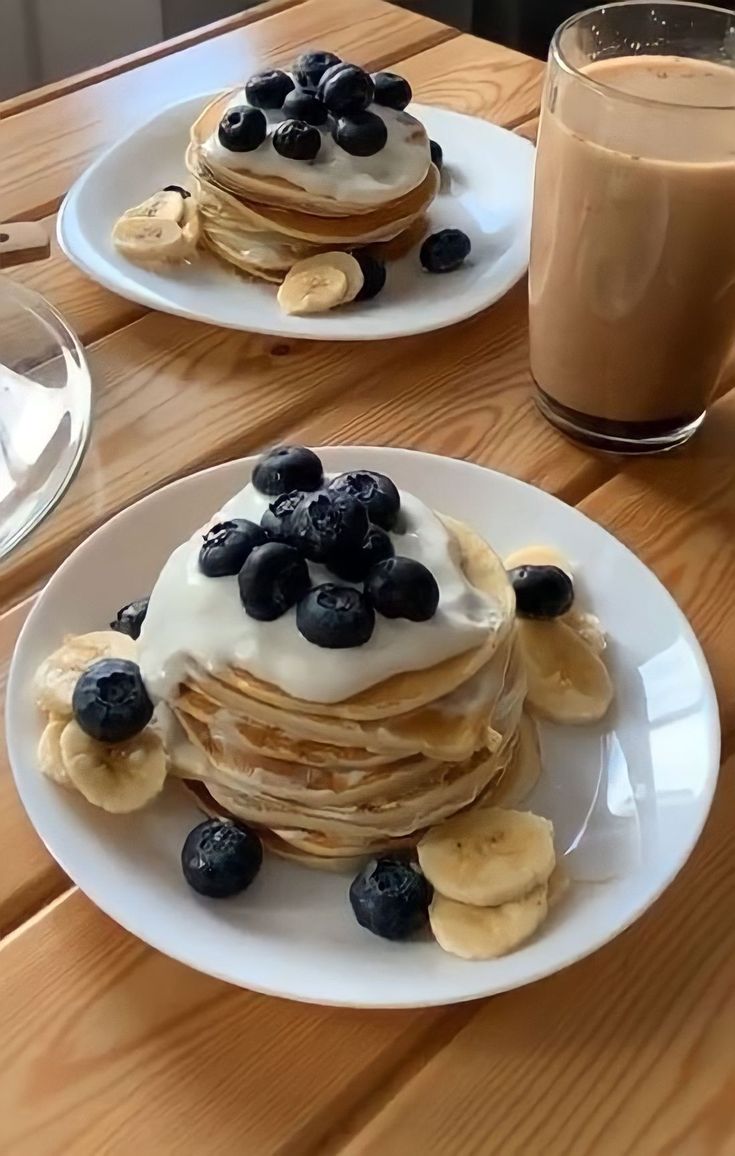 two white plates topped with pancakes and blueberries next to a glass of milk on a wooden table