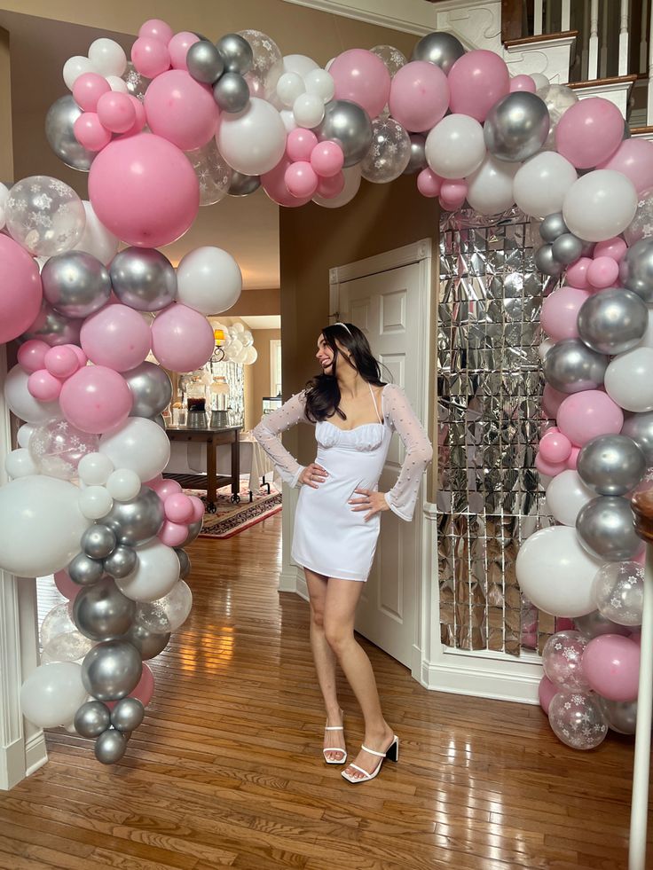 a woman standing in front of a balloon arch with pink, silver and white balloons