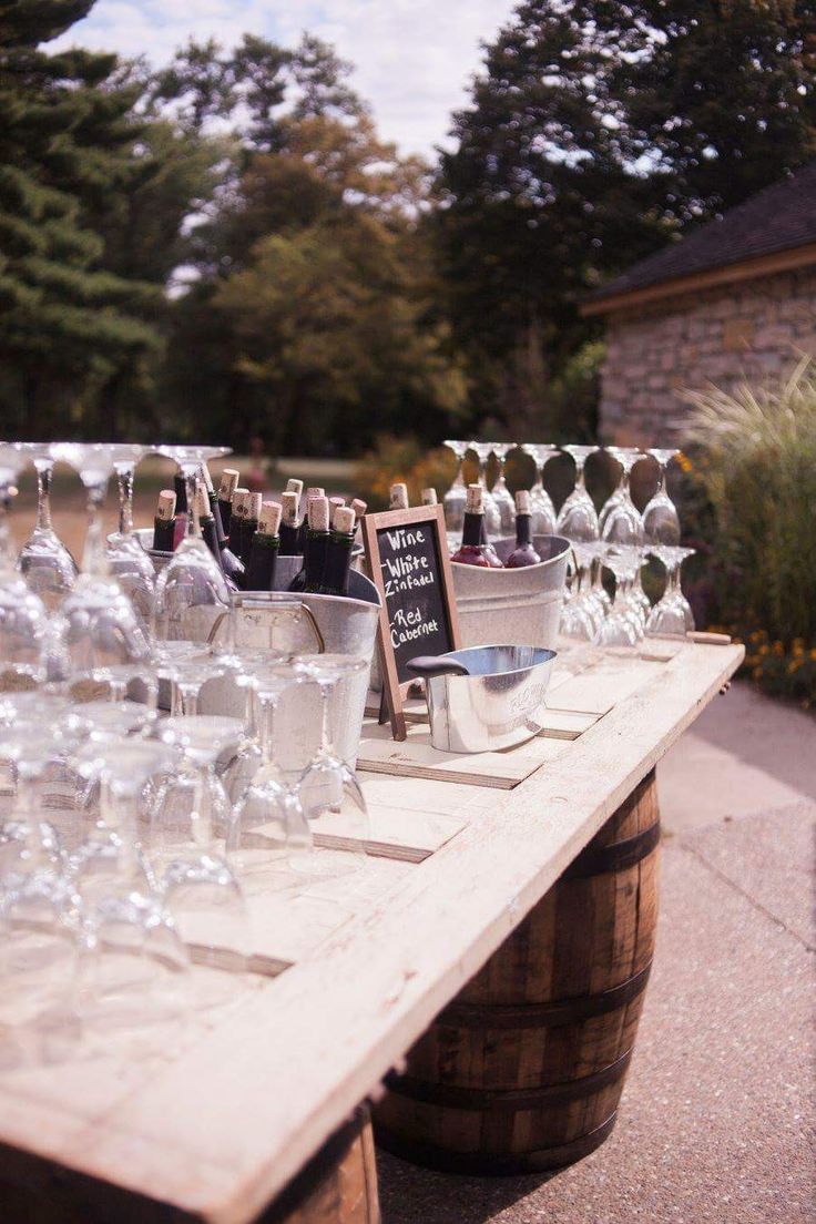 wine glasses and bottles are lined up on an outdoor table with a chalkboard sign