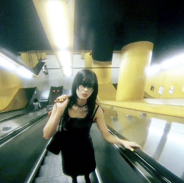 a woman riding down an escalator in a black dress