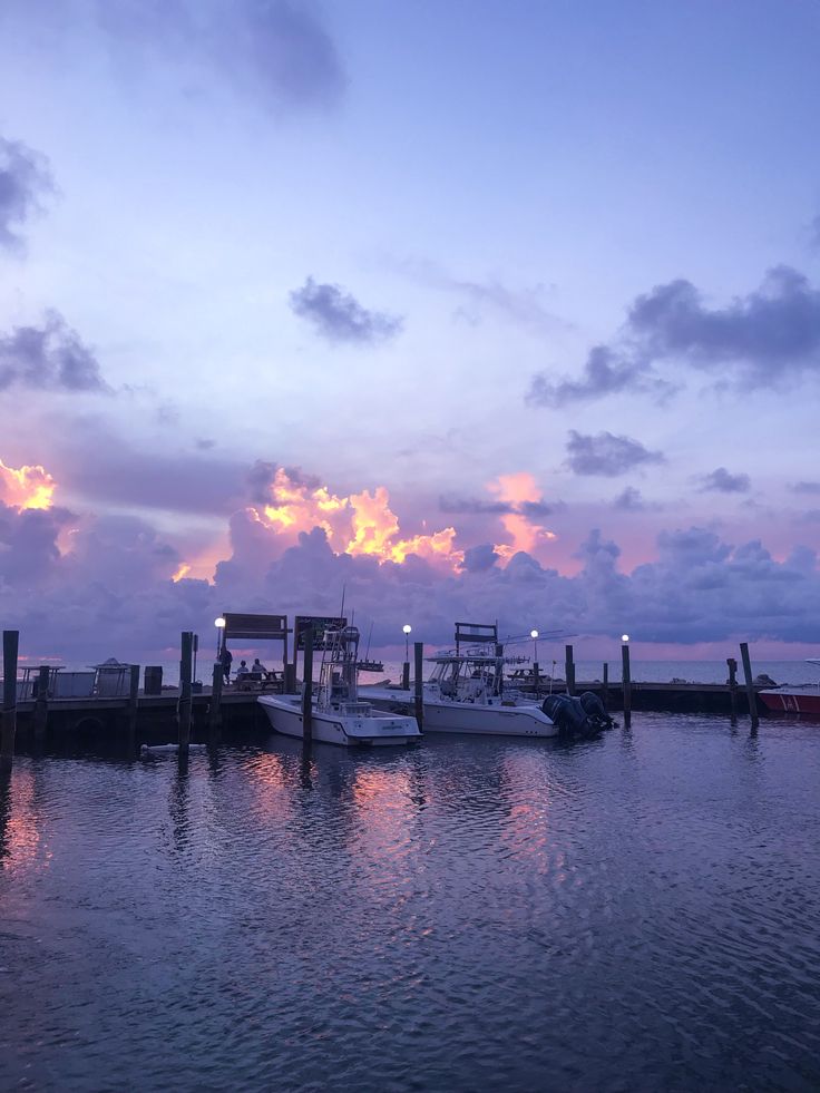 several boats are docked in the water at sunset or sunrise time with clouds above them