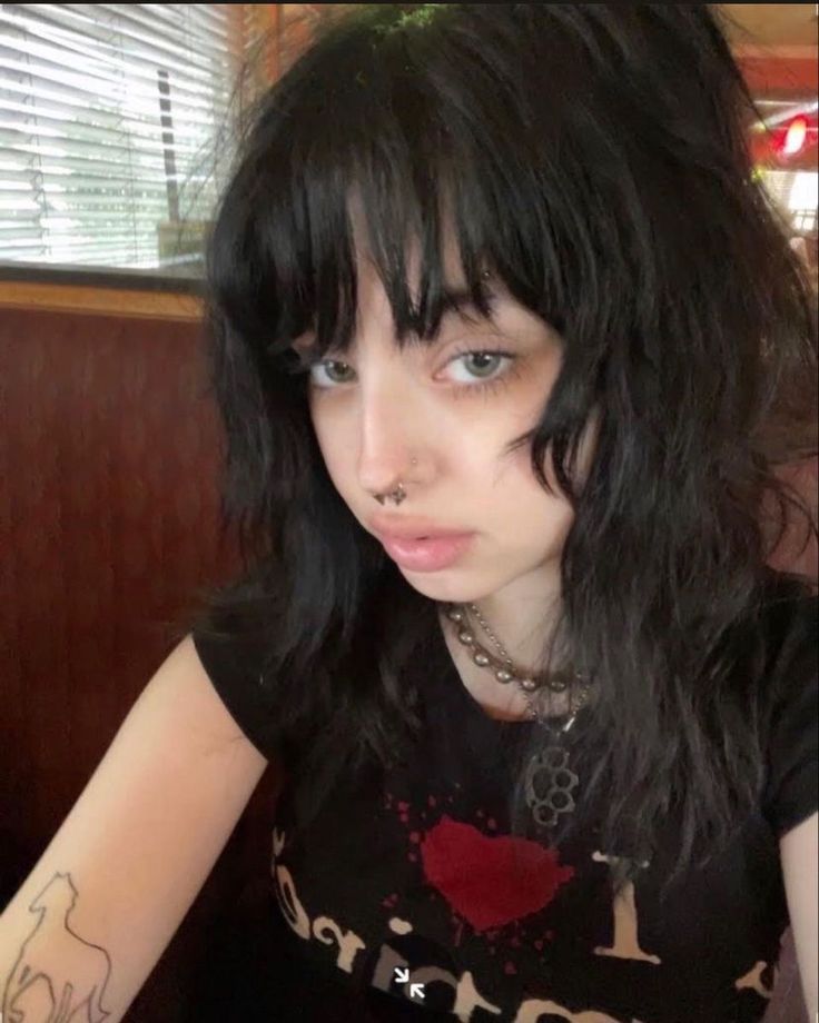 a woman with black hair and piercings on her face sitting in a booth at a restaurant