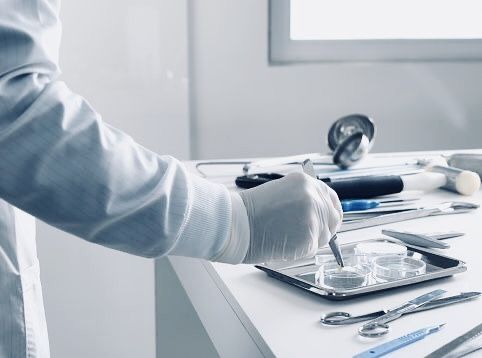 a person in a lab coat and gloves holding a spoon over a tray with tools on it