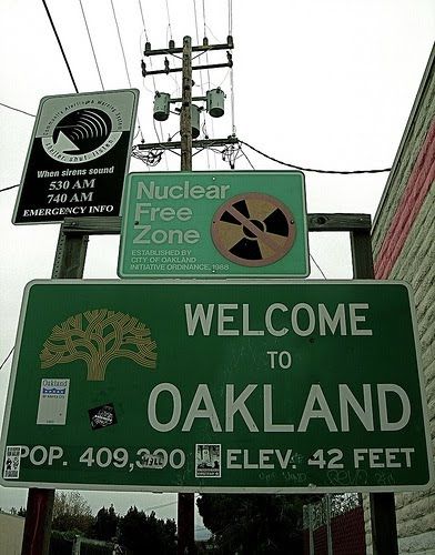 a welcome to oakland street sign in front of a brick building with power lines above it