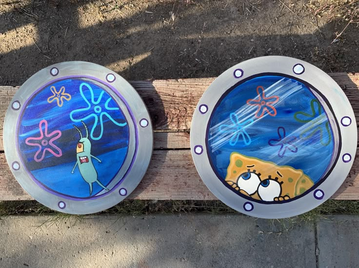 two round glass plates with cartoon images on them are sitting on a wooden bench outside