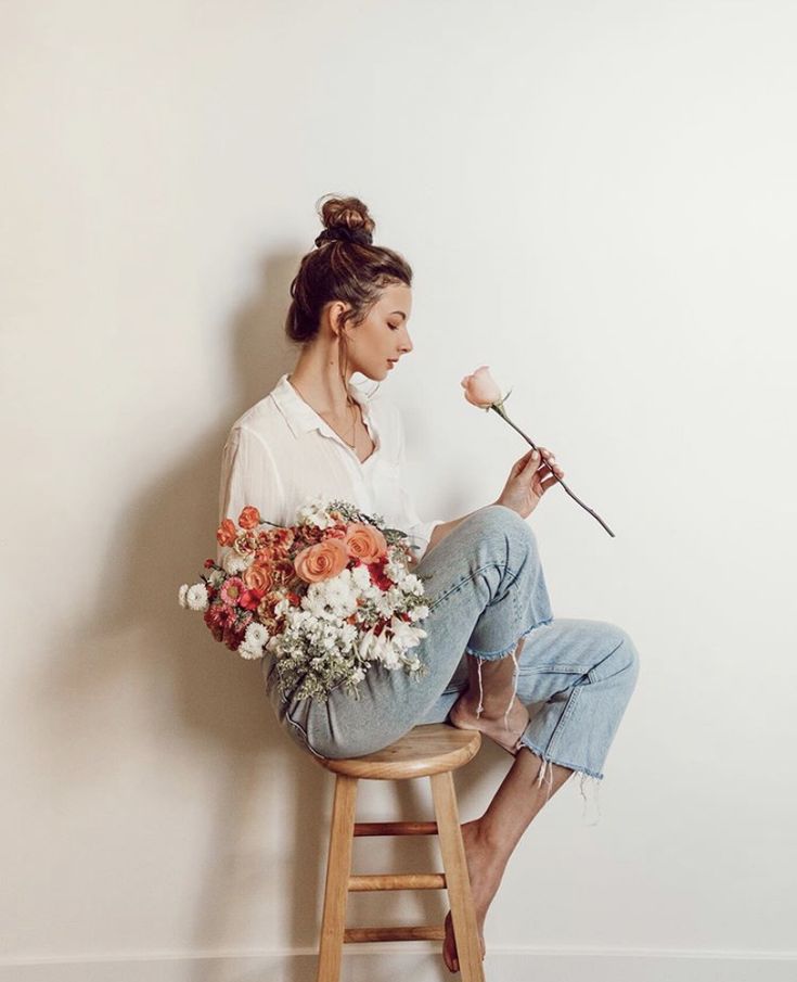 a woman sitting on a stool holding flowers